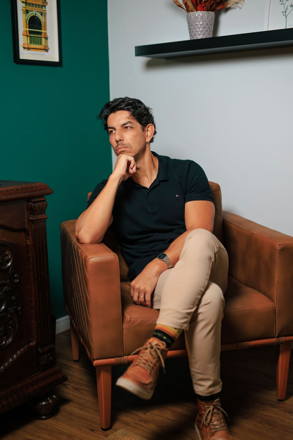 Fred Dias sentado em uma poltrona de couro, com a mão no queixo, ao lado de um móvel de madeira entalhada.
